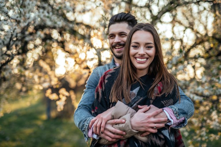 A happy couple embrace in a sunlit forest as they smile at the camera. Couples therapy and marriage counseling in Pasadena, CA can help your relationship thrive. Contact a couples therapist for more info on infidelity counseling in Pasadena, CA and other services. 95814 | 95688 | 95765