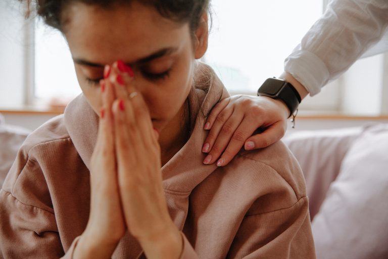 A young woman sits with her hands together over her mouth as a hand comforts their shoulder. A trauma therapist in Sacramento, CA can help in times of need. Contact a trauma therapist for support with PTSD treatment in Pasadena, CA today. 91101 | 90026 | 90042 | 90065
