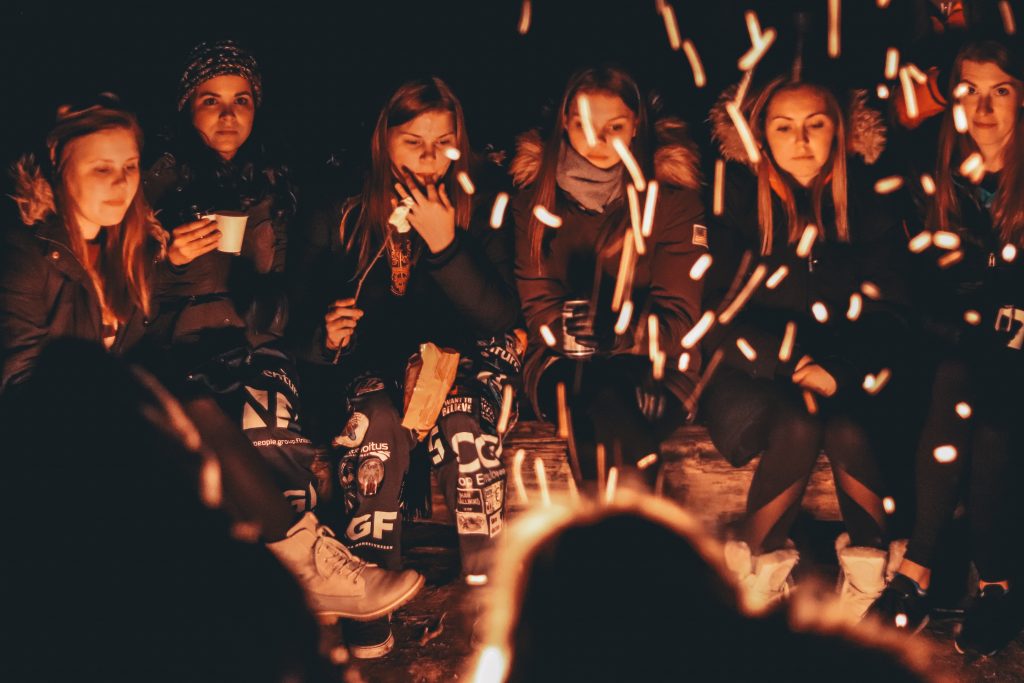 A group of woman sit around a campfire as they roast marshmallows. This represents group therapy in Pasadena, CA. Contact us today to learn more about our sexual abuse support group, group trauma therapy, and other services!