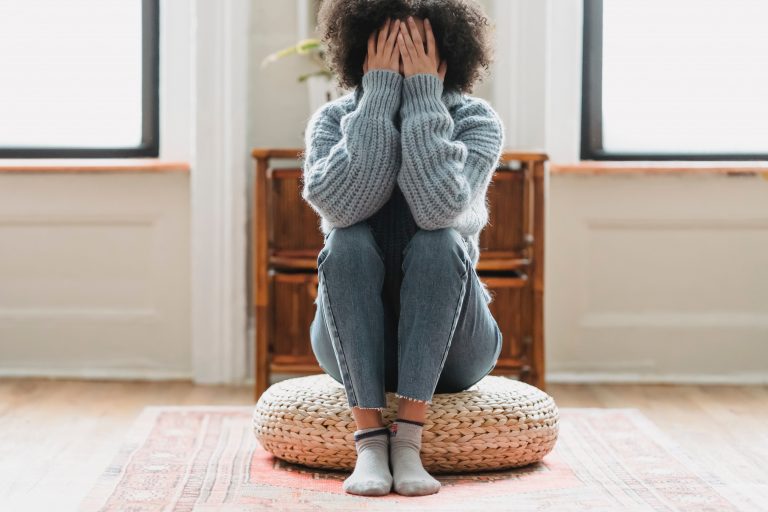 A woman sits on a floor cushion with her hands hiding her face. This could represent when online depression therapy in California can support you from home. Contact a depression therapist for support with depression treatment in Sacramento, CA and other services. 95814 | 95688 | 95765