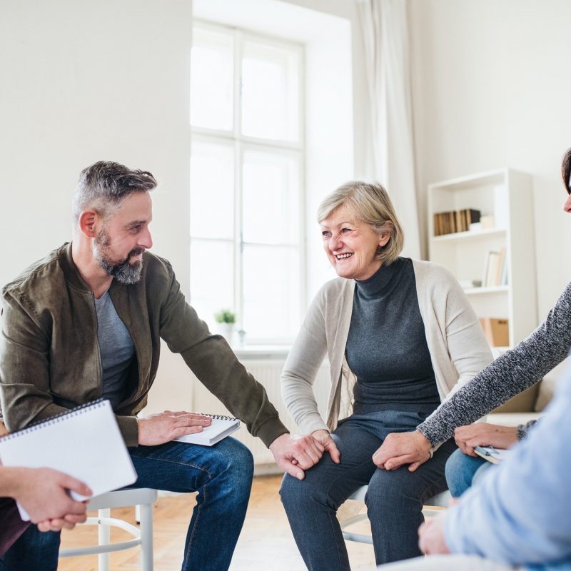 smiling group | group therapy in pasadena, ca | lgbtq support group in sacramento, ca | sexual abuse support group | 90026 Men and women sitting in a circle and holding hands and smiling. This could represent group therapy in Pasadena, CA. Contact us to learn about group trauma therapy, LGBTQ support groups, and other services to help you!